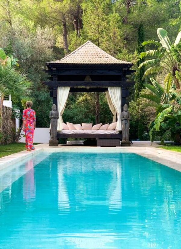 Woman in pink clothing walking towards a dark wooden day bed by the pool at TNM's Ibiza Retreat.