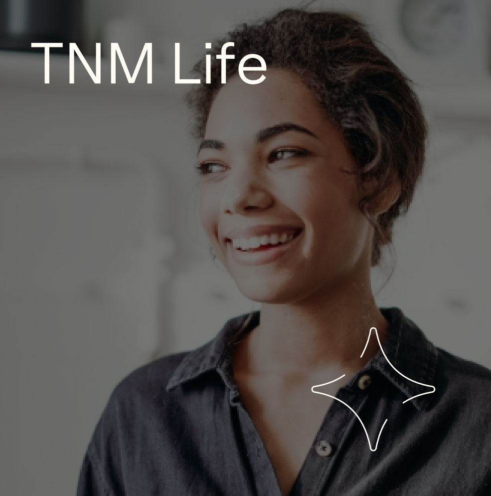 A woman at a TNM Life event with dark hair pulled back and blue shirt smiles to someone off camera.