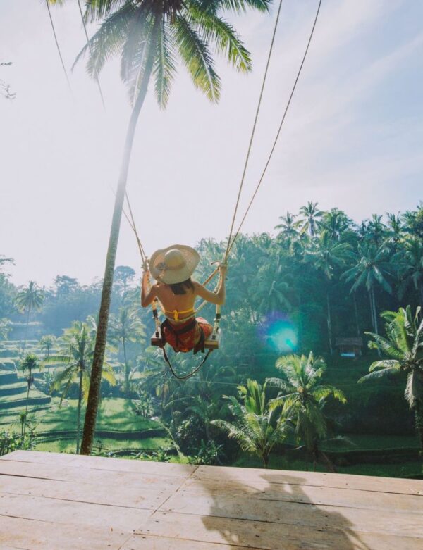 Woman in a sarong and straw hat on a giant swing at the TNM retreat overlooking the rice fields of Bali.