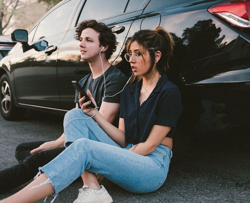 A man and woman leaning against a car listening to a TNM self-growth podcast